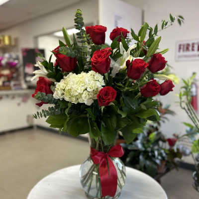 Red roses and white hydrangea in a glass vase with a red ribbon