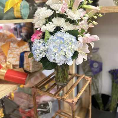 Mixed bouquet of lilies, hydrangeas, and white daisies in a glass vase