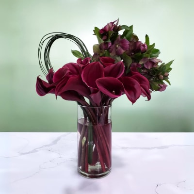 Deep burgundy calla lilies and purple flowers in a clear glass vase