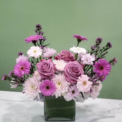 Pink and lavender roses with daisy-like flowers in a square glass vase
