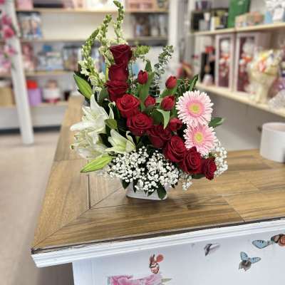 Red roses, white lilies, and pink daisies in a white vase