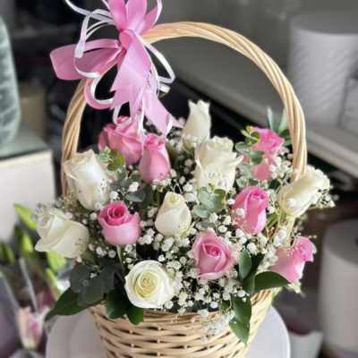 Pink and white roses arranged in a wicker basket with a ribbon bow