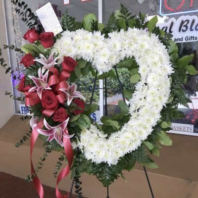 Heart-shaped floral wreath with white chrysanthemums, red roses, and pink lilies on an easel