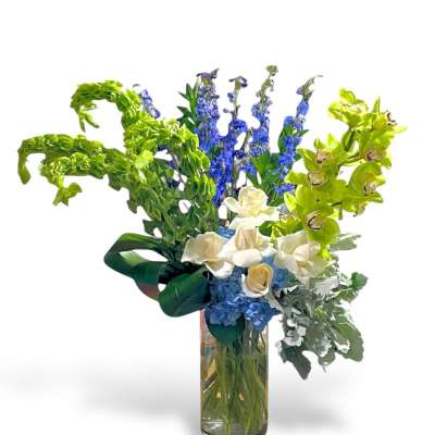 Tall bouquet of blue, white, and green flowers in a glass vase