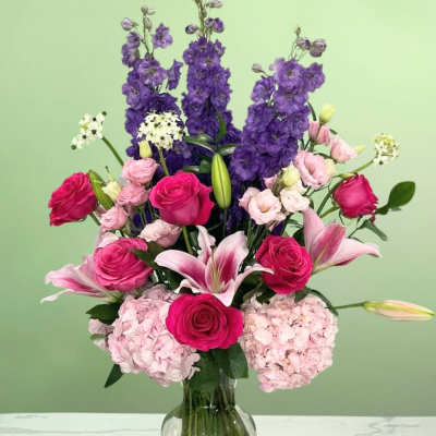 Pink roses and lilies in a glass vase with tall purple blooms