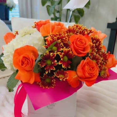Orange roses and burgundy daisies in a white gift box with a pink ribbon.