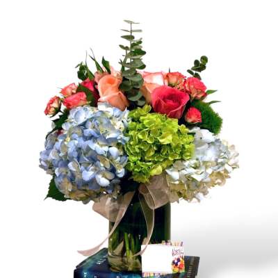 Bouquet of hydrangeas and roses in a glass vase with books underneath