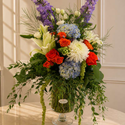 Tall mixed bouquet in a glass vase with purple, blue, white, and orange flowers