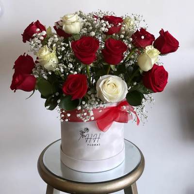 Red and white roses arranged in a white hat box with a red ribbon