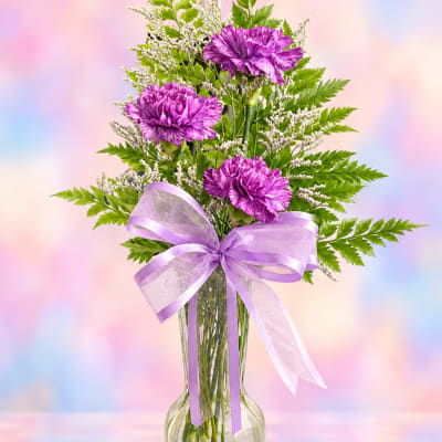 Purple carnations in a clear vase with a lavender ribbon bow