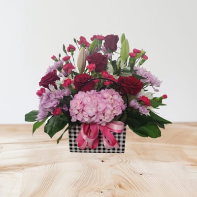 Pink and red flower arrangement in a checkered basket with ribbon