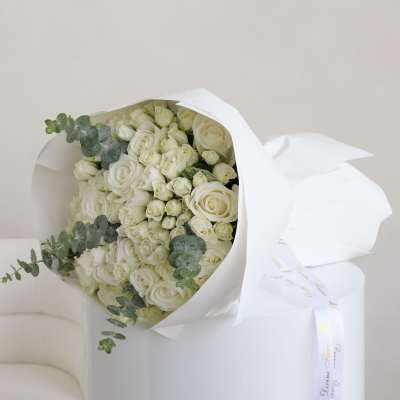 Bouquet of white roses wrapped in white paper with eucalyptus