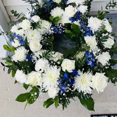 White roses and chrysanthemums arranged in a circular wreath with blue flowers