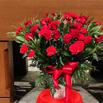 Red roses and carnations arranged in a vase with a red ribbon