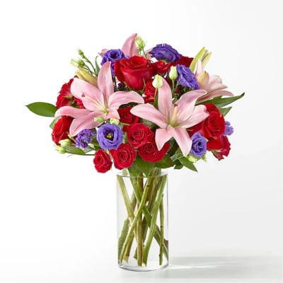 Bouquet of red roses, pink lilies, and purple blooms in a clear glass vase