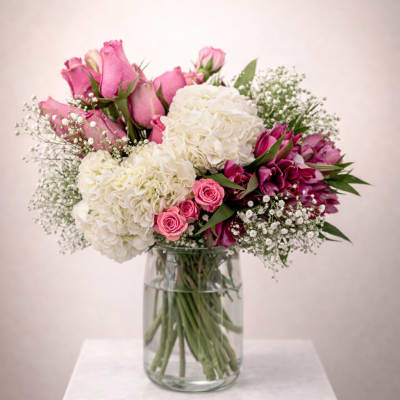 Pink roses, white hydrangeas, and magenta blooms arranged in a clear glass vase