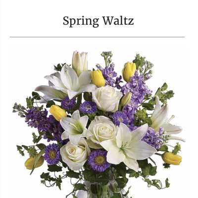 White lilies, roses, and purple flowers in a clear glass vase