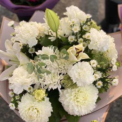 White bouquet with lilies, carnations, and daisies wrapped in pale paper