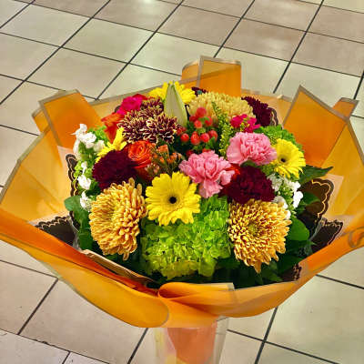 Colorful mixed bouquet in orange wrap with a tall clear vase