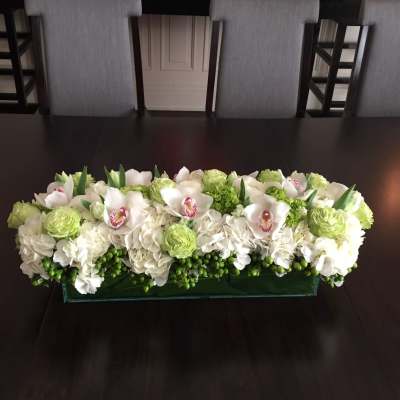 Low rectangular floral arrangement with white orchids, hydrangeas, and green blooms