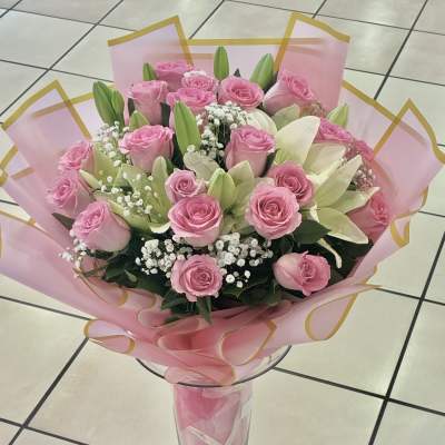 Hand-tied bouquet of pink roses, white lilies, and baby's breath wrapped in pink paper.