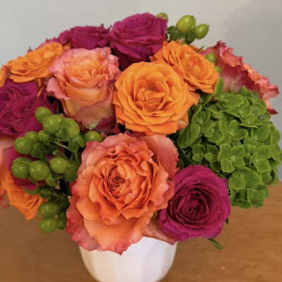 Bouquet of orange, pink, and magenta roses in a white vase