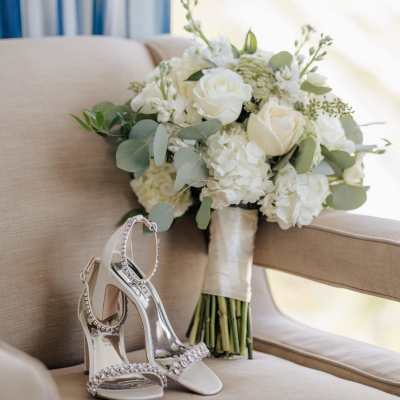 White rose bouquet with greenery beside jeweled high-heeled sandals