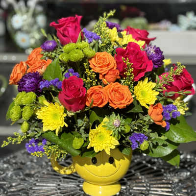 Mixed bouquet in a yellow smiley-face vase with roses and mums