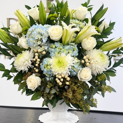 White roses, lilies, hydrangeas, and mums in a white pedestal vase