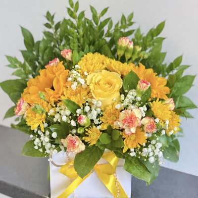 Yellow and orange flower arrangement in a white box with a yellow ribbon
