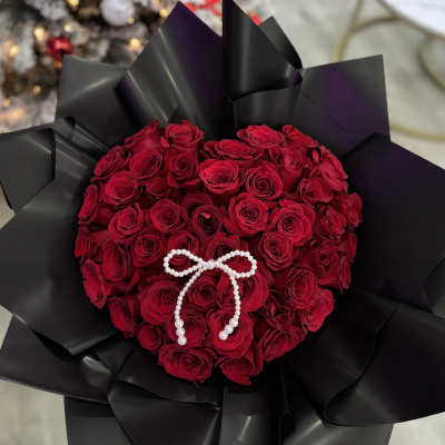 Heart-shaped bouquet of red roses with a pearl bow on black wrap