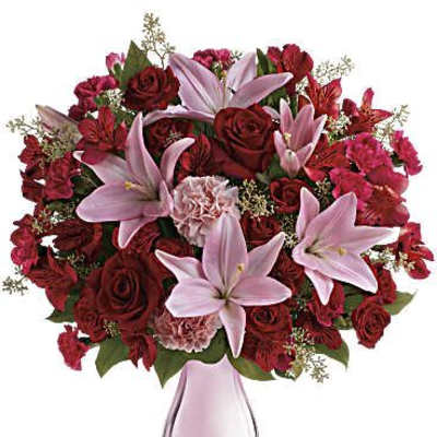 Pink lilies and red roses arranged in a pink glass vase