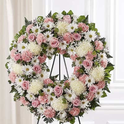 Pink and white floral wreath on a black stand