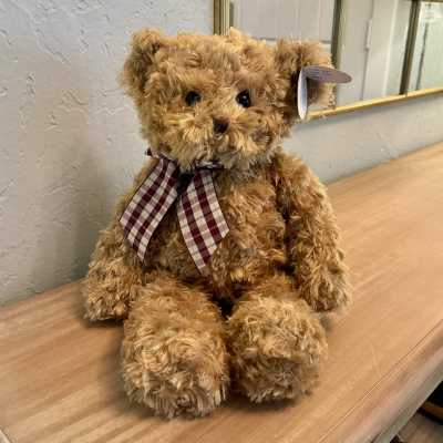 Plush teddy bear with a plaid ribbon sitting on a wooden surface