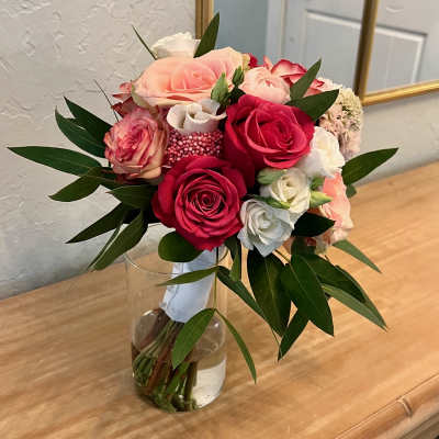Hand-tied bouquet of pink and red roses with white blooms in a clear glass vase