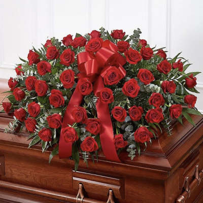 Red rose casket spray with a large red ribbon on a wooden casket