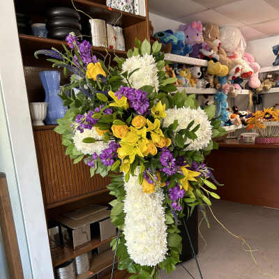 Standing floral cross with white chrysanthemums, yellow roses, and purple flowers
