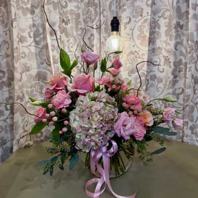 Pink floral arrangement with hydrangeas, roses, and a ribbon in a glass vase