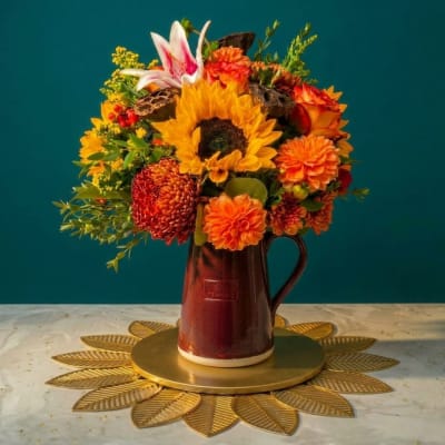 Sunflower and orange flower arrangement in a burgundy pitcher vase