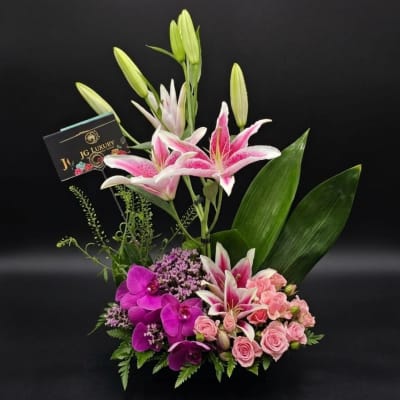 Pink lilies and orchids arranged with roses in a vase