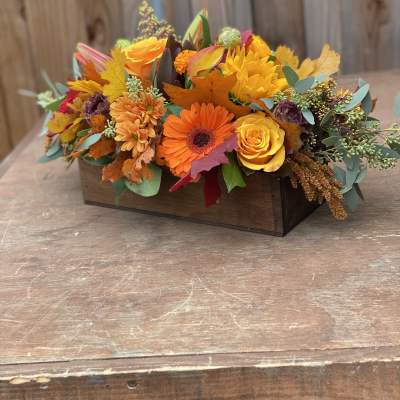 Autumn floral arrangement in a wooden box with orange and yellow blooms