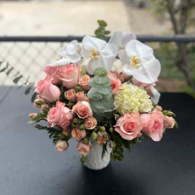 Pink roses and white orchids arranged in a white vase