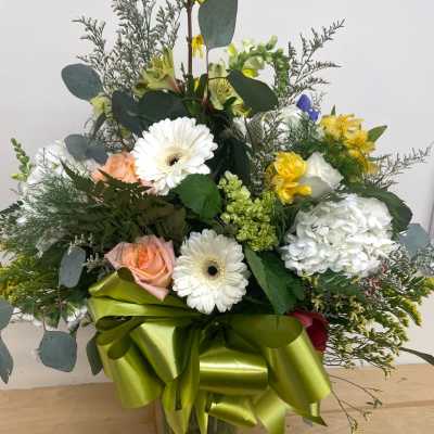 Mixed bouquet with white daisies, roses, hydrangea, and a green ribbon in a glass vase