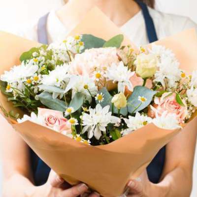 Bouquet of white daisies and pale pink roses wrapped in tan paper