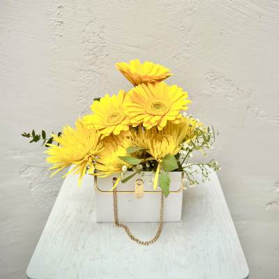 Yellow gerbera daisies in a white box with a gold chain handle