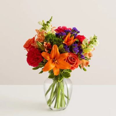 Colorful bouquet of lilies, roses, and carnations in a clear glass vase