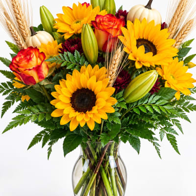 Sunflower and rose bouquet with lilies and pumpkins in a glass vase