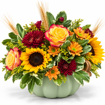 Mixed bouquet in a pale green pumpkin vase with sunflowers and roses