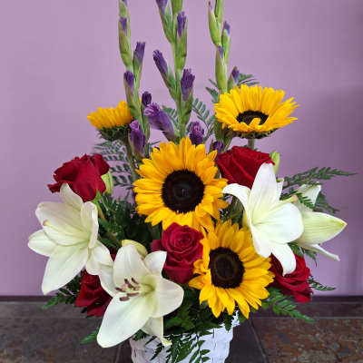 Basket arrangement with red roses, white lilies, and yellow sunflowers