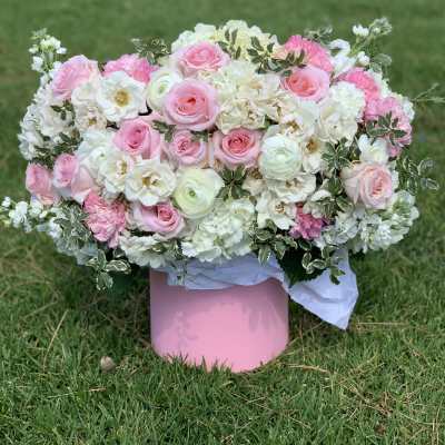 Pink and white floral arrangement in a pink box on grass